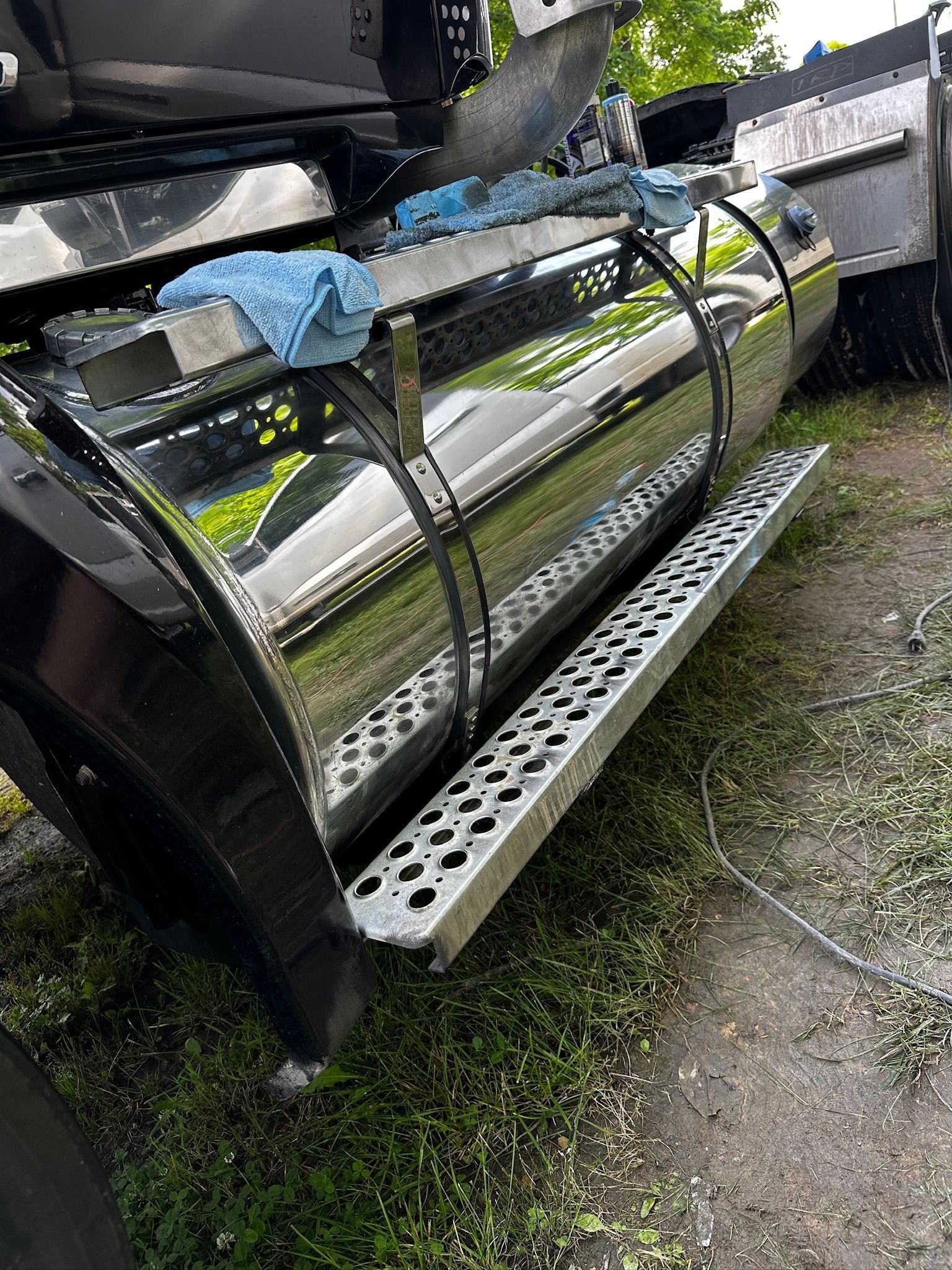 A black truck with a stainless steel fuel tank is parked in the grass.