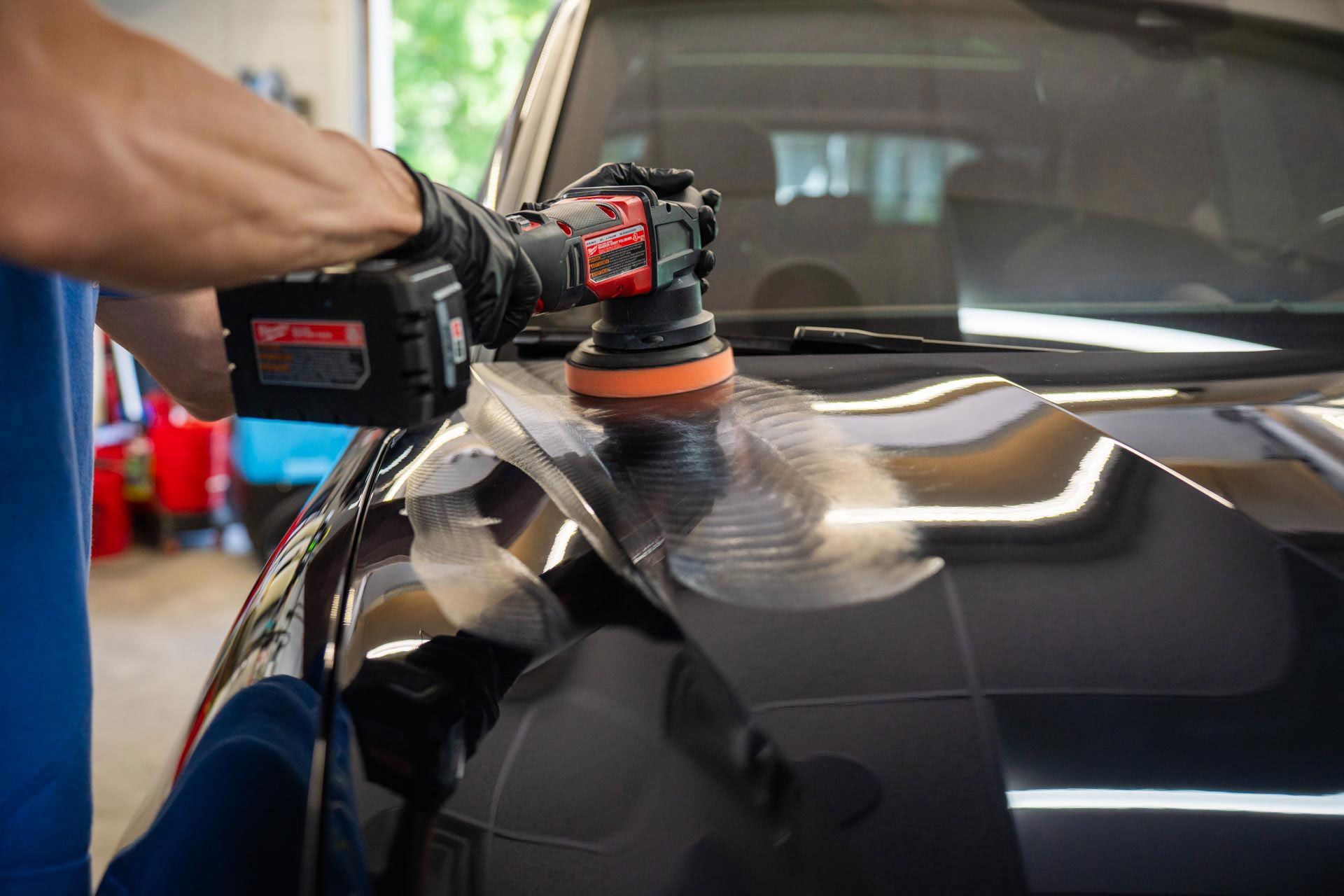 A man is polishing the hood of a car with a machine.